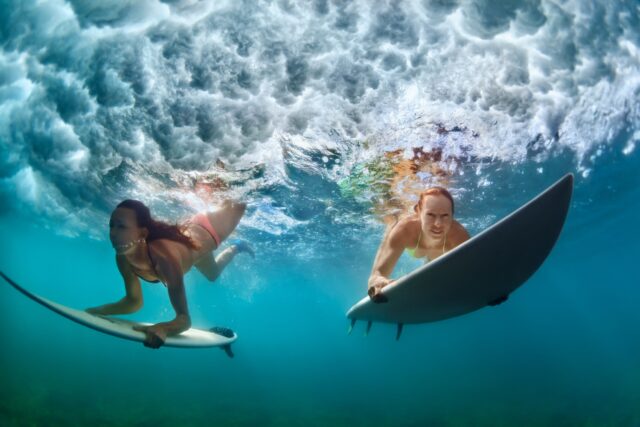 Surfer women with surf board dive underwater under breaking big wave