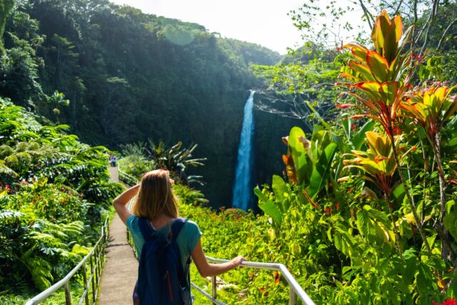 Woman hiker stands on the path and watches waterfall in the tropical forest
