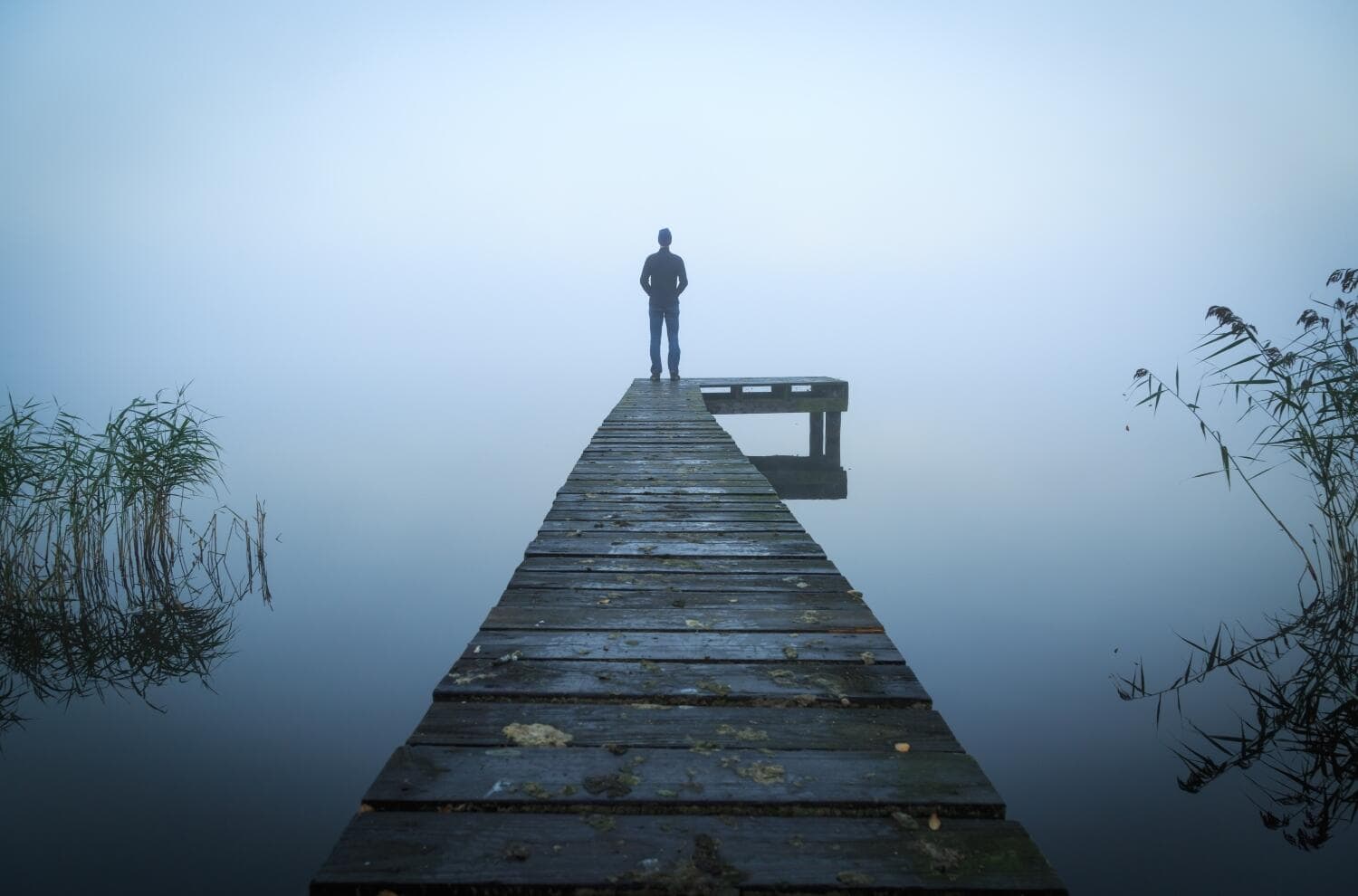 Isolation Concept. Man standing on the ledge Man standing on a jetty at a lake during a foggy, gray morning.