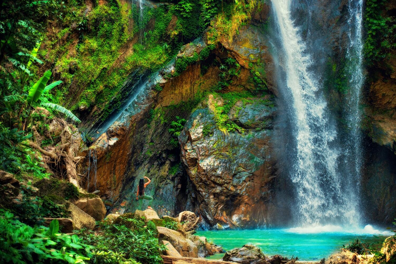 Nature Immersion Concept. Young woman standing on a rock near a waterfall