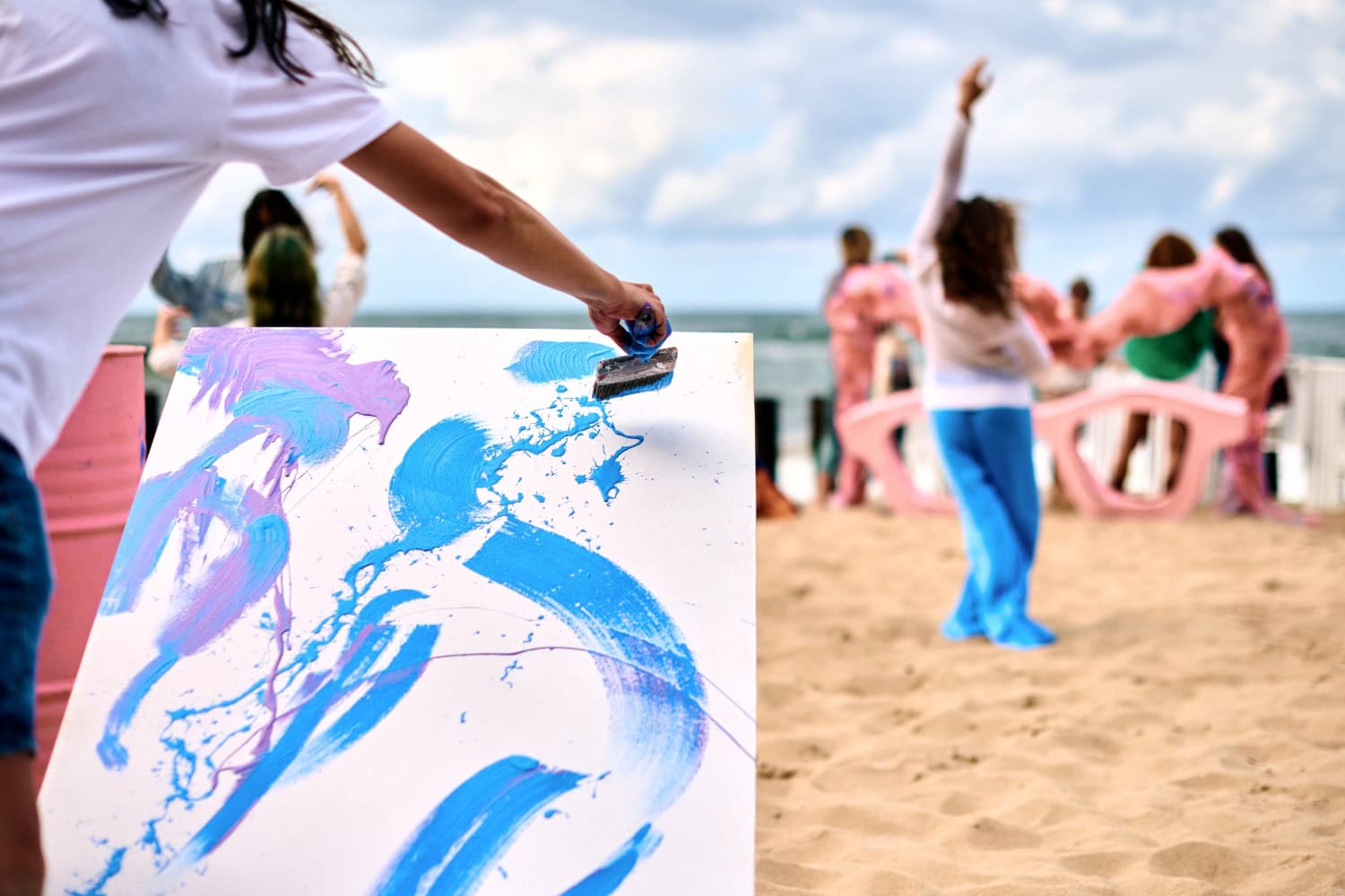 Drip painting outdoor art performance with dancing girls on sandy sea beach. Painter artist drawing on white canvas abstract picture in drip painting abstract art technique. Creative art festival