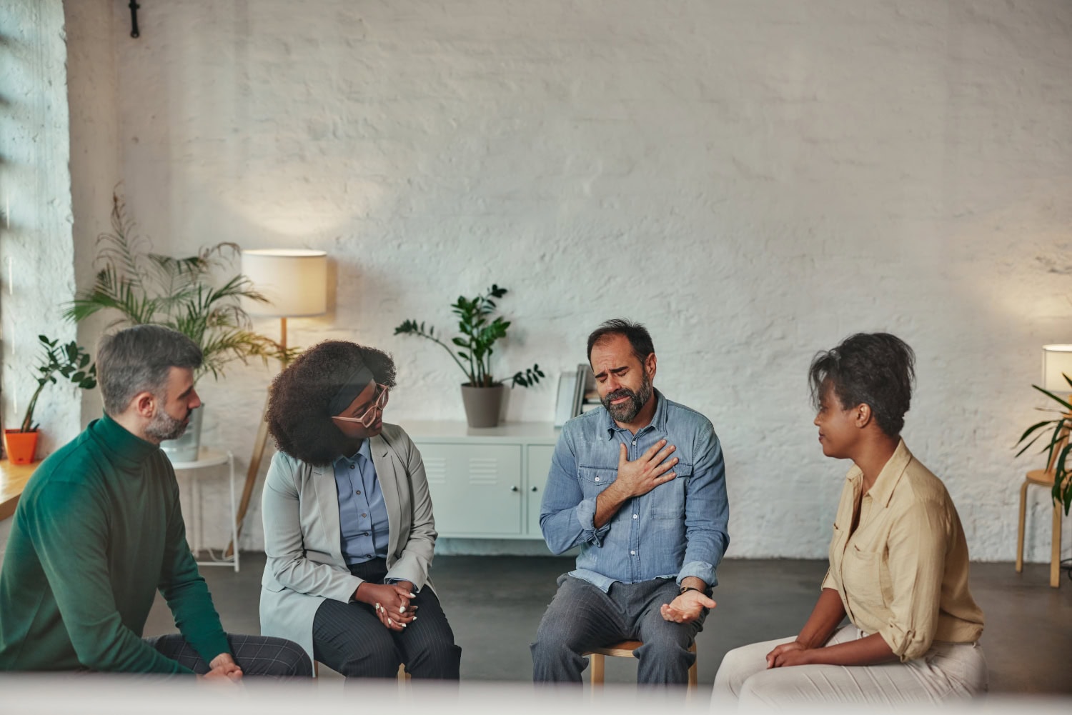 A multiracial group of therapy session at a medical office. Participants and the group therapist provide support to a sad man who confided to group
